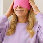 Woman smiling while wearing a pink sleep mask over her eyes and a lavender sweatshirt.