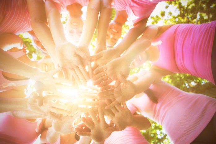 Group of people in pink shirts join hands in a circle, showing teamwork outdoors.