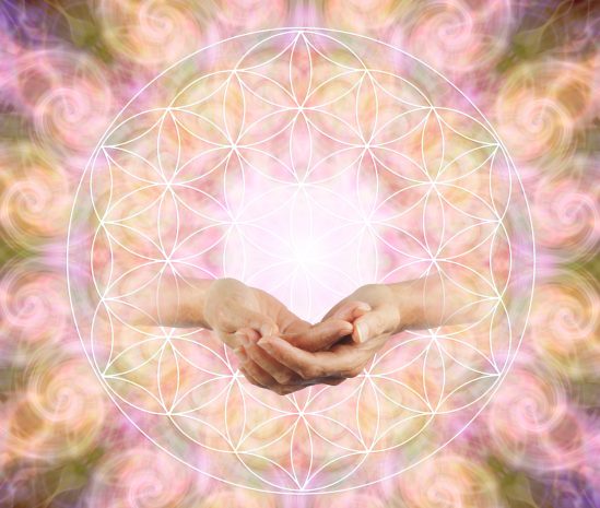 Two hands cupping a white Flower of Life geometric pattern against a soft pink–orange, swirled background.